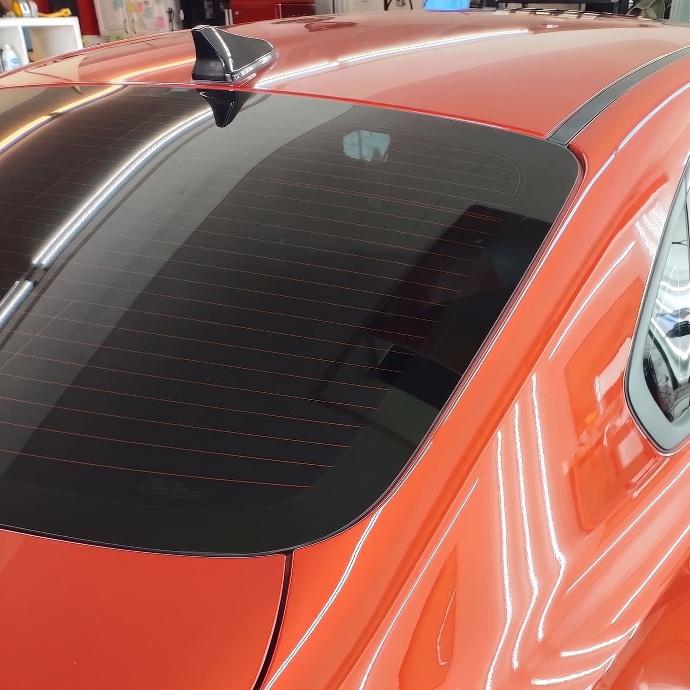 Finished dark tint on the rear window of a glossy orange sedan in the Luxe Tint bay, the film running right to the edge of the glass